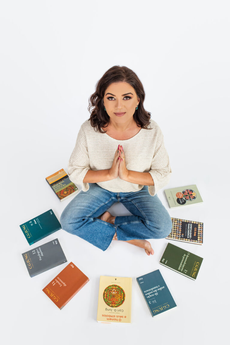 Malu Monteiro sentada, com as mãos unidas, cercada por livros de Carl Jung